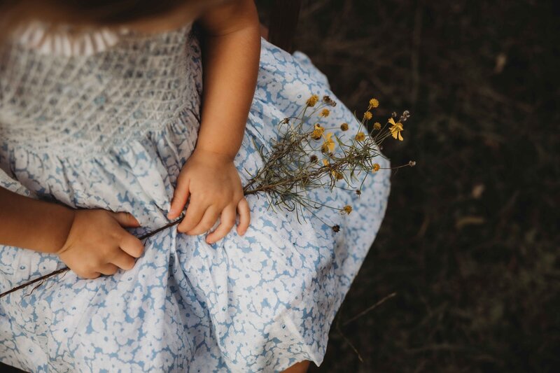 Tiny toddler fingers curled around a flower stem during a lifestyle family session