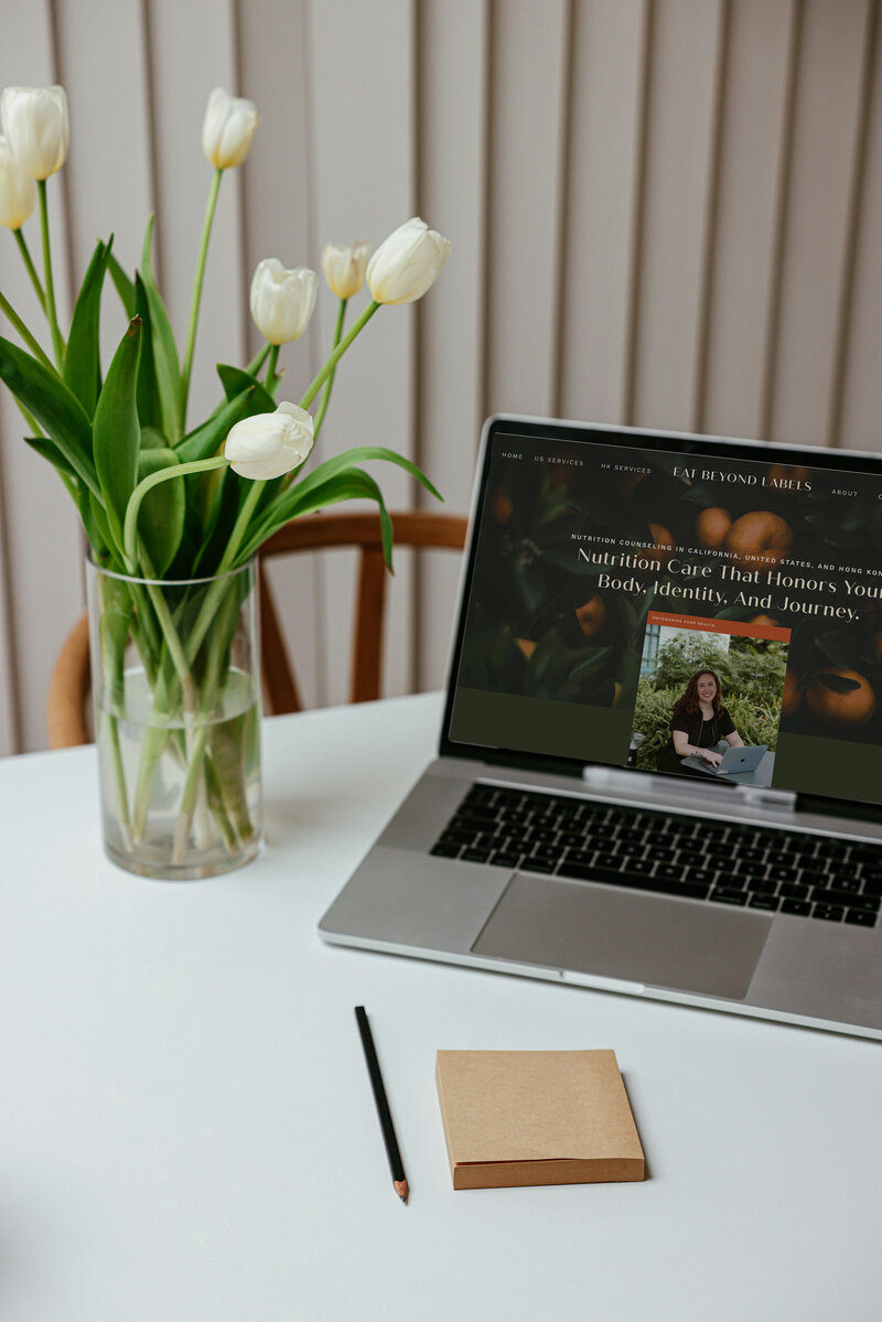 A desk featuring a laptop and a vibrant vase of tulips, perfect for an inclusive nutritionist's creative environment.