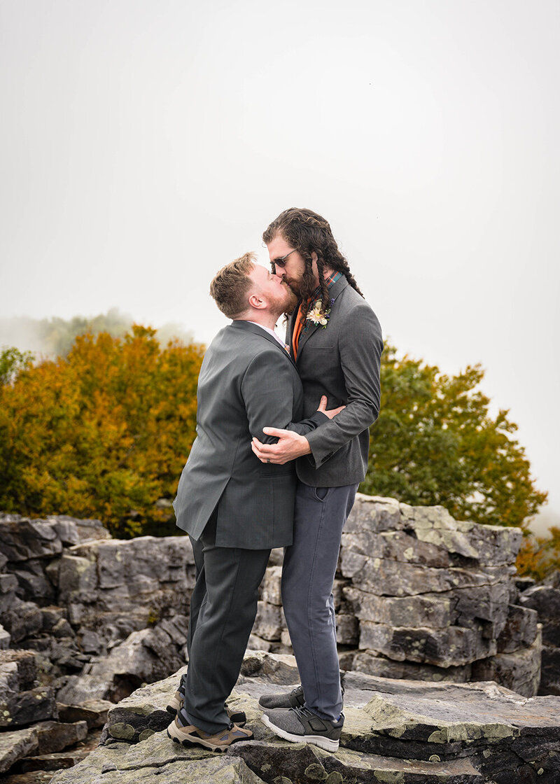 A gay couple kiss atop a large mountain of rocks on their elopement wedding day at Shenandoah National Park.