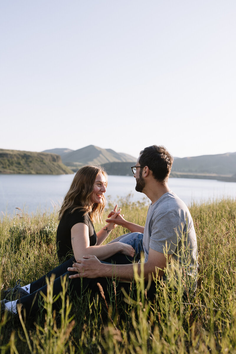 Couple laughing together while sitting in the grass with views of Lucky Peak Lake in Boise, Idaho