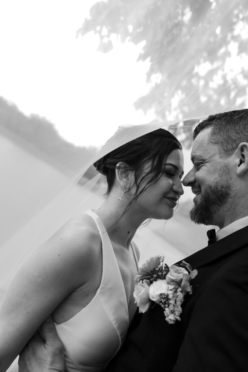 Romantic close-up of the bride and groom under the wedding veil, sharing a tender moment with soft light and delicate details.