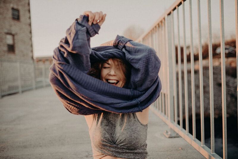 A woman pulls a purple sweater off over her head while laughing.
