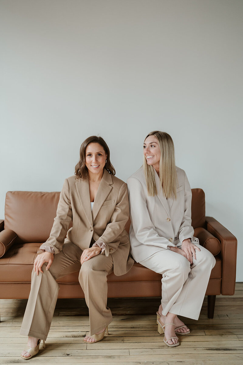 Two women sitting on couch, neutral business suits, brand photos, marketing agency branding, social media strategists, social media management