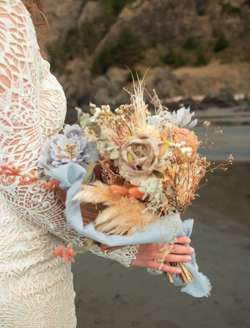 A beautiful moment of a bride and groom sharing a kiss on a sandy beach, with gentle waves rolling in and the sun casting a warm glow over the scene. The couple stands close, framed by the serene ocean and a soft horizon. Photo taken by Kollar photography Arizona Elopement photographer