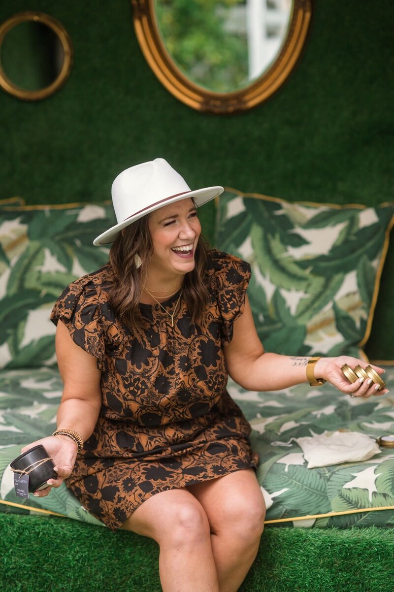 Chasity Campbell laughing headshot wearing white hat holding candles with green background