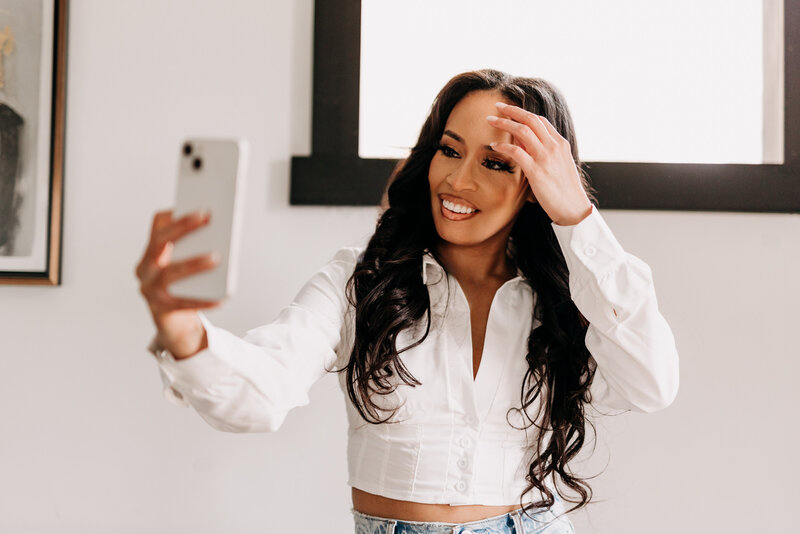 Tiara in a white top holding up her iPhone taking a selfie