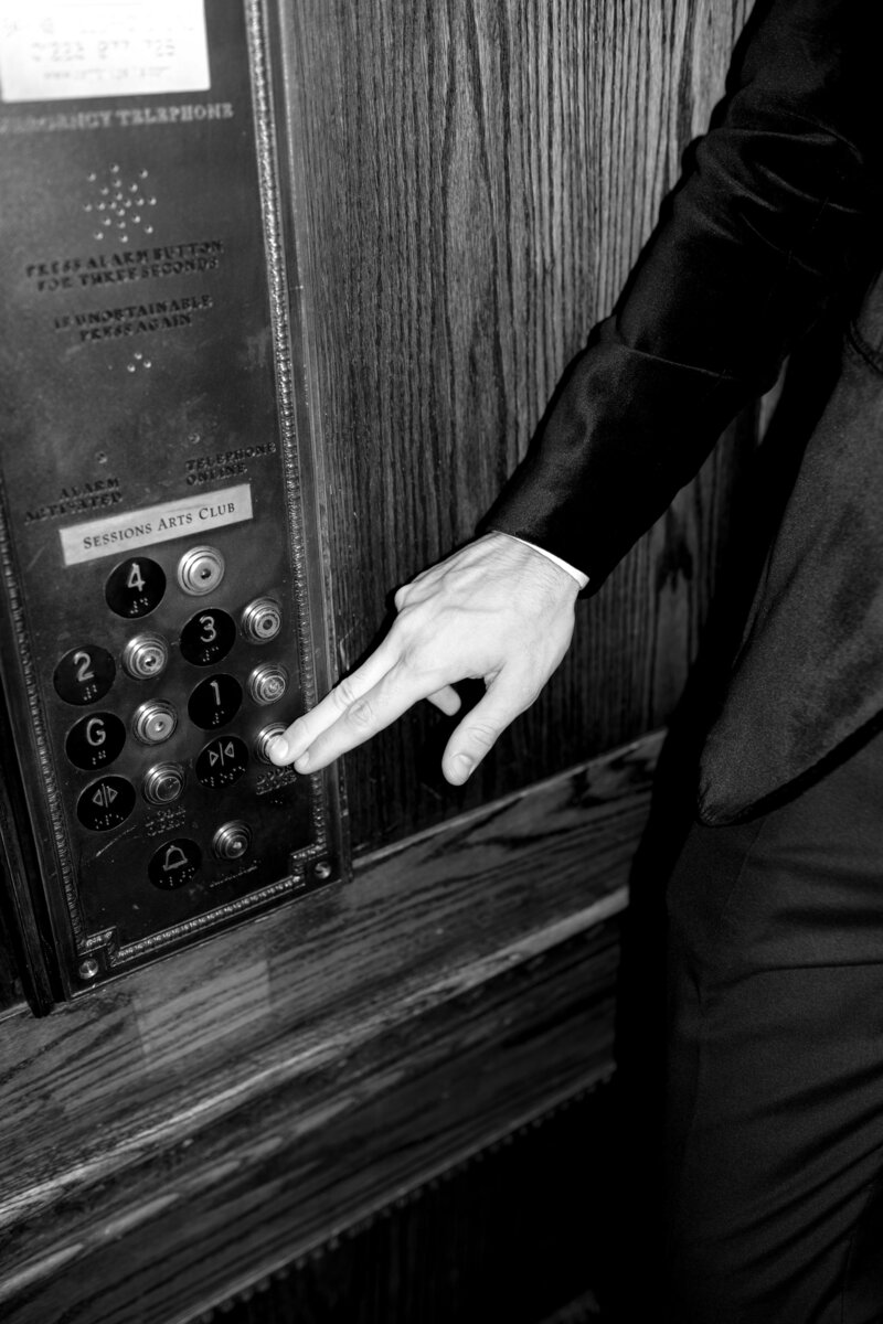 Groom pressing lift button at Sessions Arts Club, dressed in tuxedo.