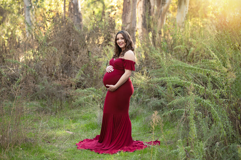Charlotte maternity photographer showcasing an elegant twilight session in a nature park. This maternity photoshoot features a mother-to-be in a flowing burgundy gown, captured in the soft glow of twilight. Specializing in natural, artistic maternity photography, I-CanDee Photography creates timeless images that highlight the beauty of motherhood. Located in Charlotte, NC, and published in leading photography magazines.