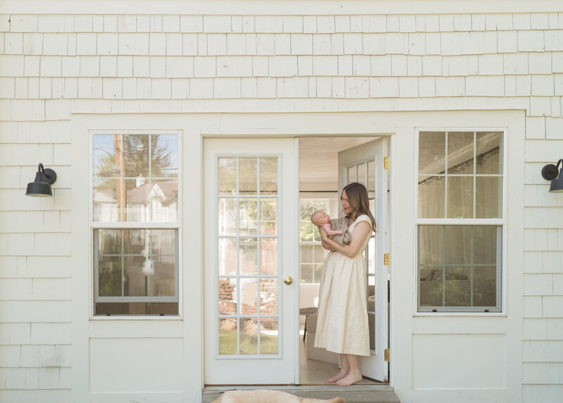 mom standing outside house holding baby 