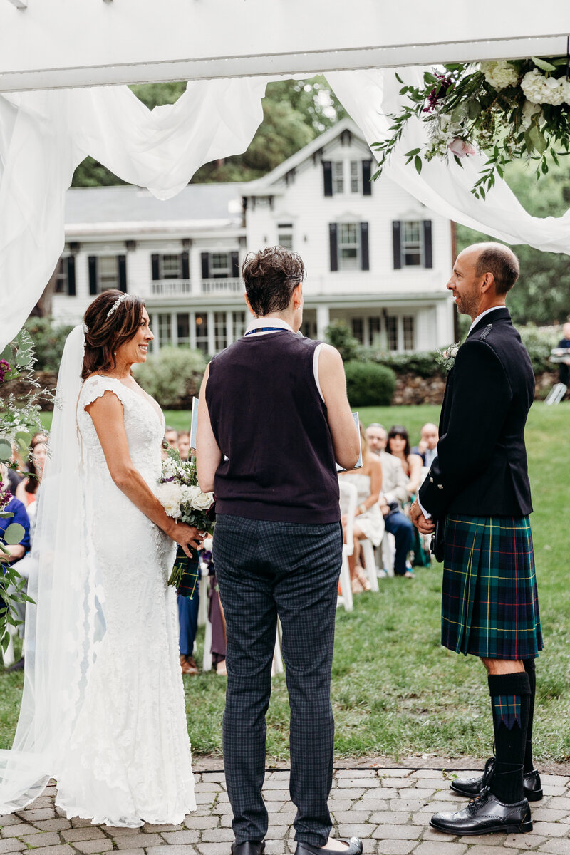 A groom in a kilt stands with his bride and officiant at the altar during their outdoor ceremony