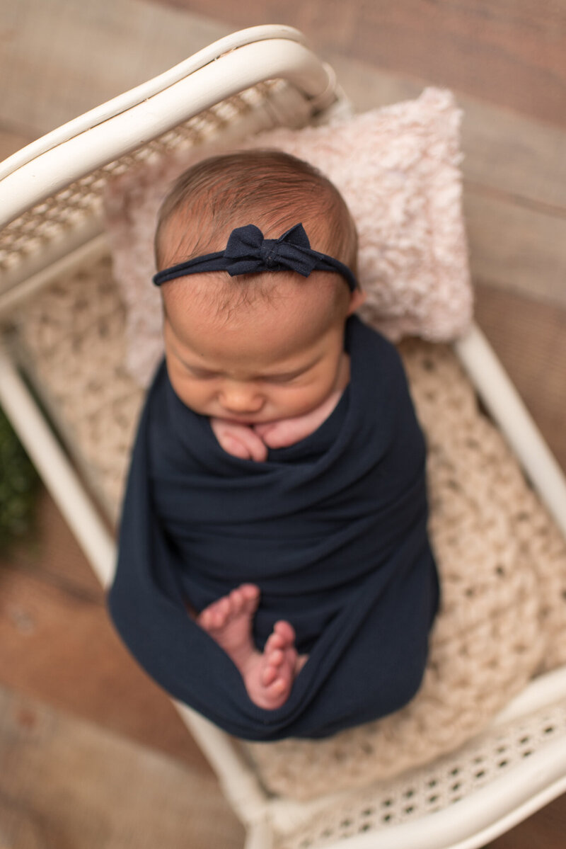 A baby girl is wrapped in navy, laying on white bed with fingers and toes sticking out