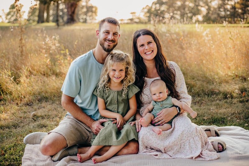 Jennifer sitting on blanket in a field with her husband and two children