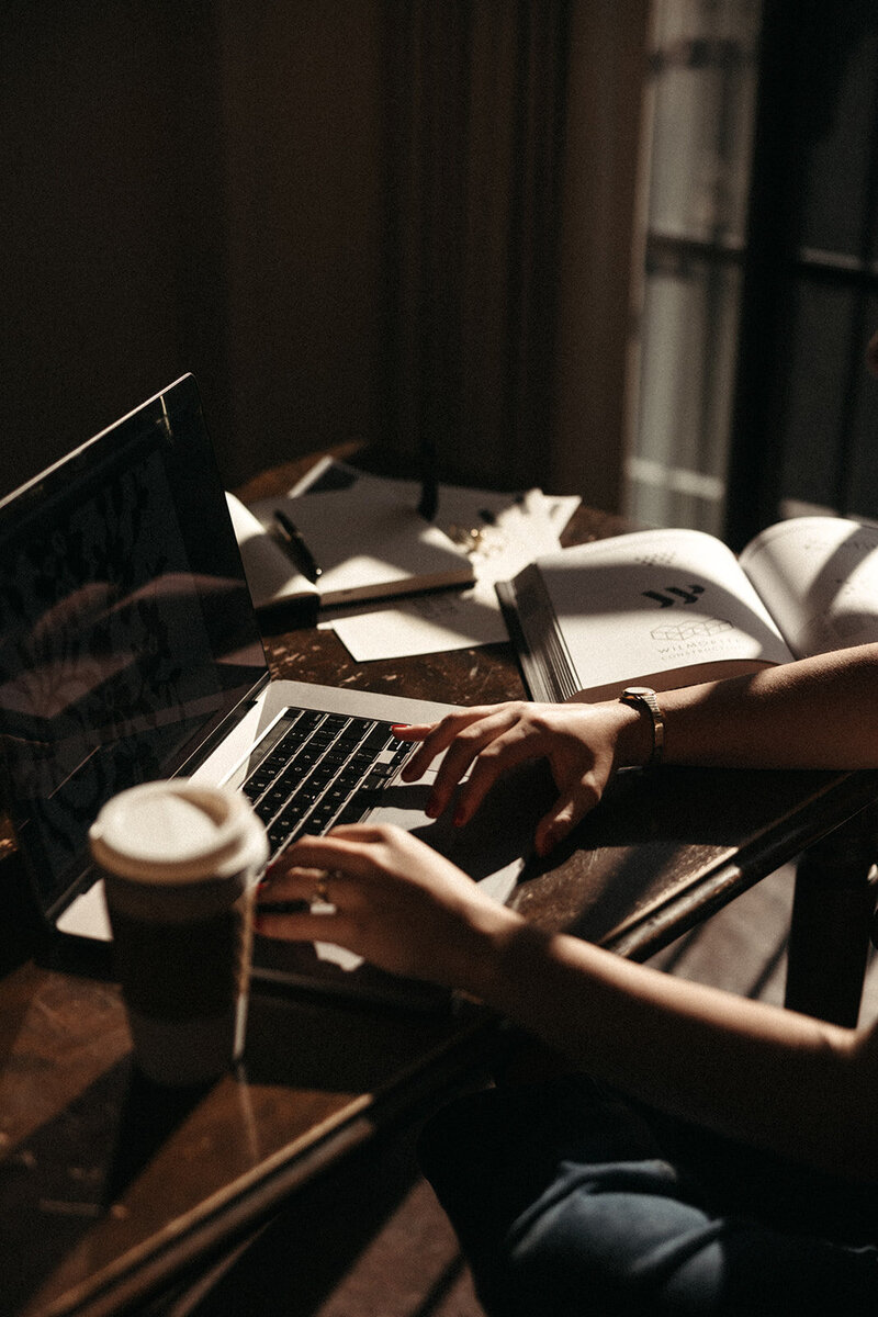 Moody image of a woman working on laptop  with coffee and notebooks sprawled on the desk