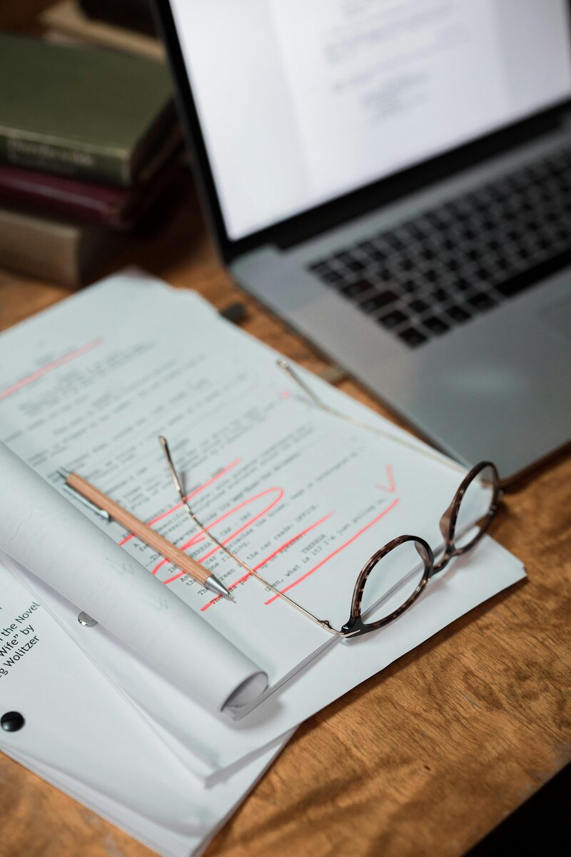 Copy editor’s workspace with marked-up manuscript, reading glasses, and laptop for professional editing and proofreading services.