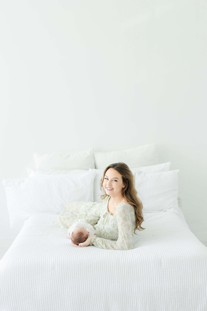 Mom laying on a bed in a dothan alabama photography studio with newborn baby during newborn photography session