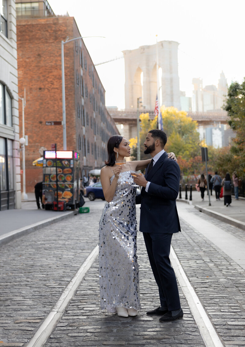 The couple stands close together under the Brooklyn Bridge in DUMBO, Brooklyn, capturing an urban charm.