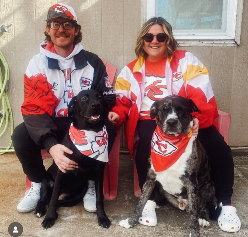 Husband and wife (owners) with their two dogs, all wearing Chiefs gear