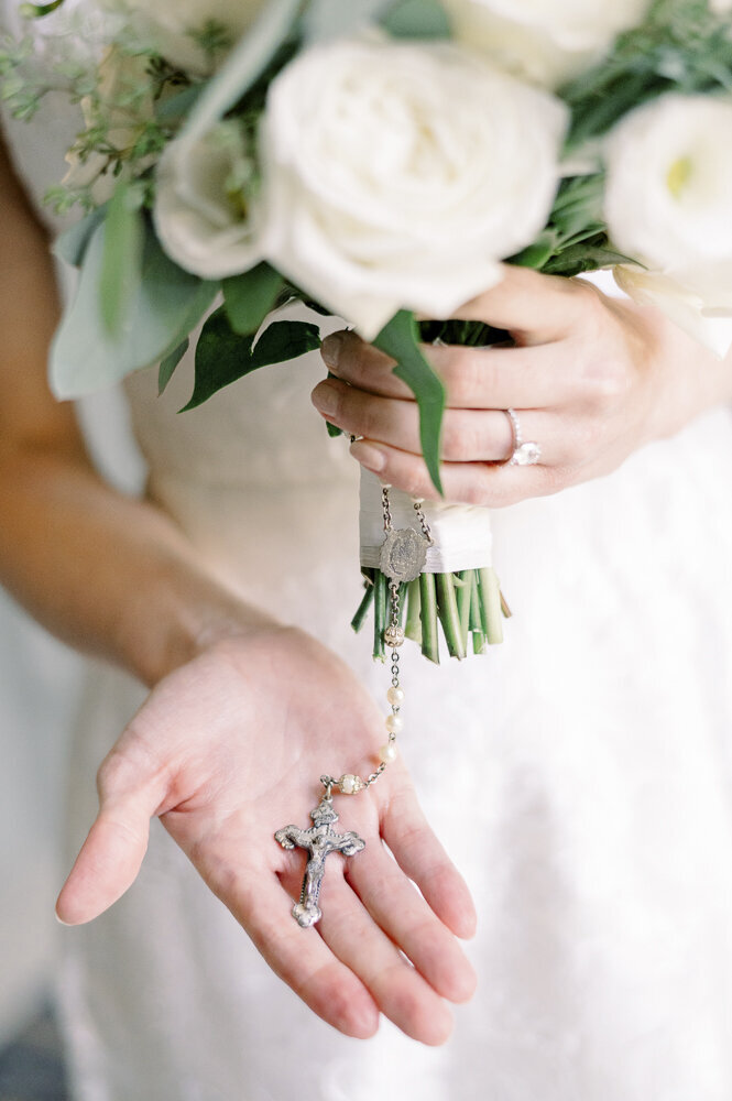 a bride holding a Catholic rosary and a bouquet