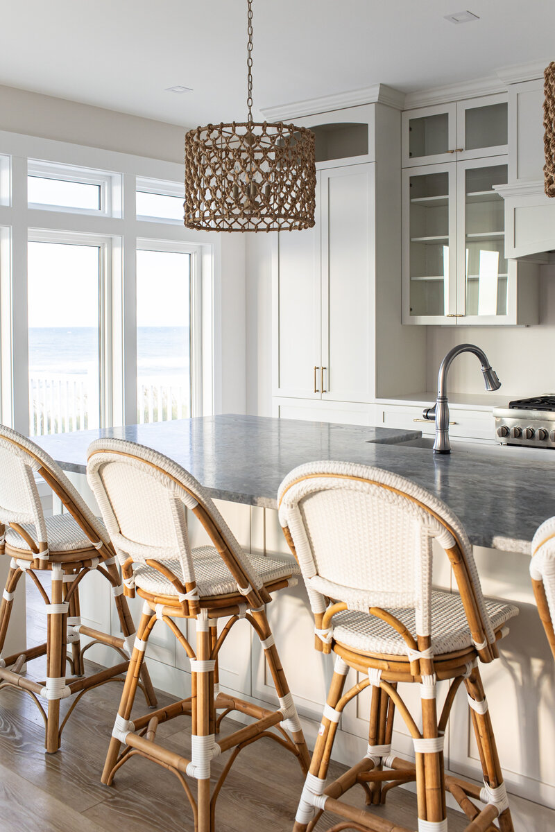 A serene kitchen nook featuring beach-inspired rattan stools and a stunning ocean view. The clean and airy design of the kitchen, combined with light editing, creates a fresh and inviting atmosphere.