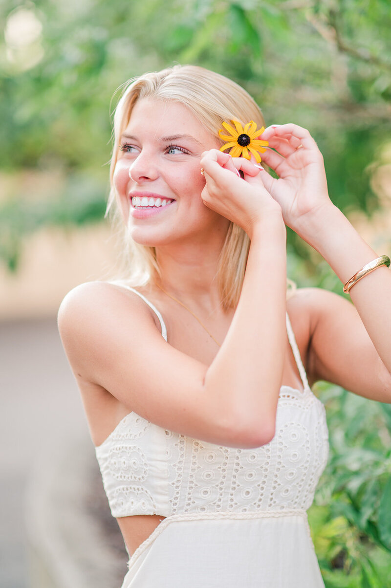 a girl smiling as she plays with a flower in her hair