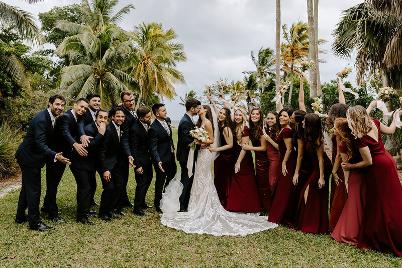 M&C Kissing surrounded by all bridesmaids and groomsmen.