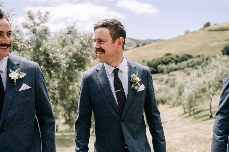 groom in grey blue suit in akaroa at mt vernon in olive trees in akaroa