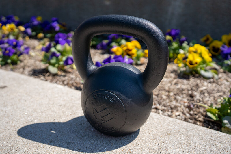 a black kettlebell sits in front of a flower bed