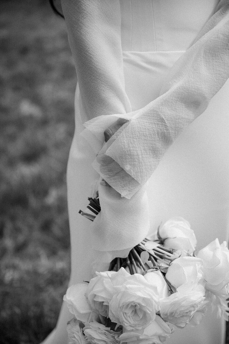 Bride Jenay standing outdoors holding a bouquet of white, mauve, and beige florals including garden roses and ranunculus, by Summer Robbins Flowers in Central Oregon