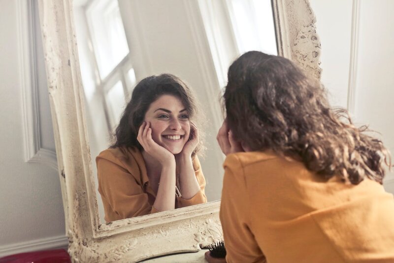 A woman smiling in the mirror because she knows the key to lasting happiness thanks to Madison therapist, Stephanie Thomas.