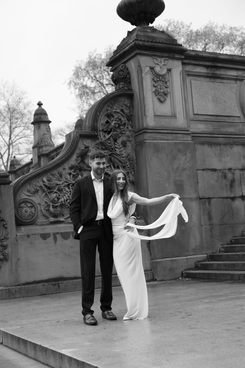 Engaged couple standing close together on the stairs at Bethesda Fountain, surrounded by the elegant architecture of Central Park.