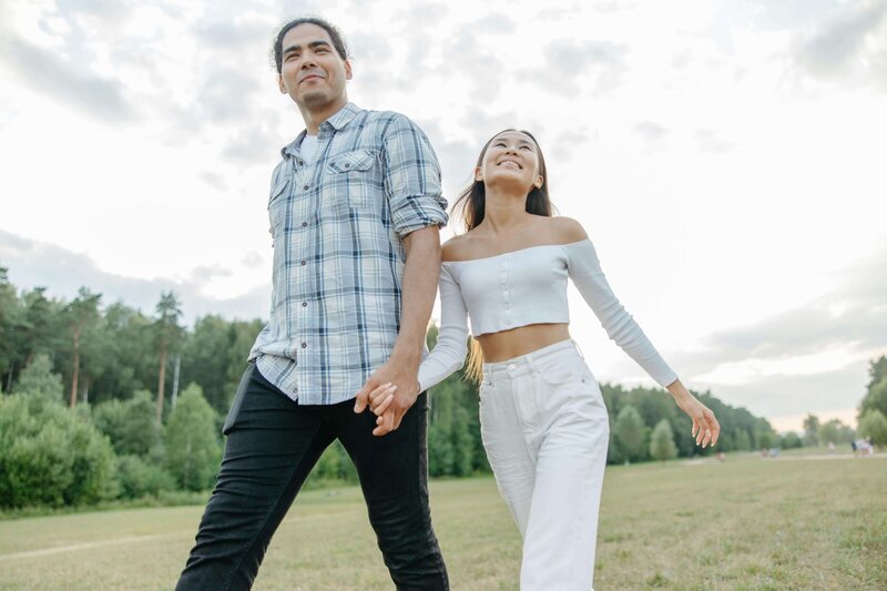 a mand and woman walking through a field smiling happily and holding hands