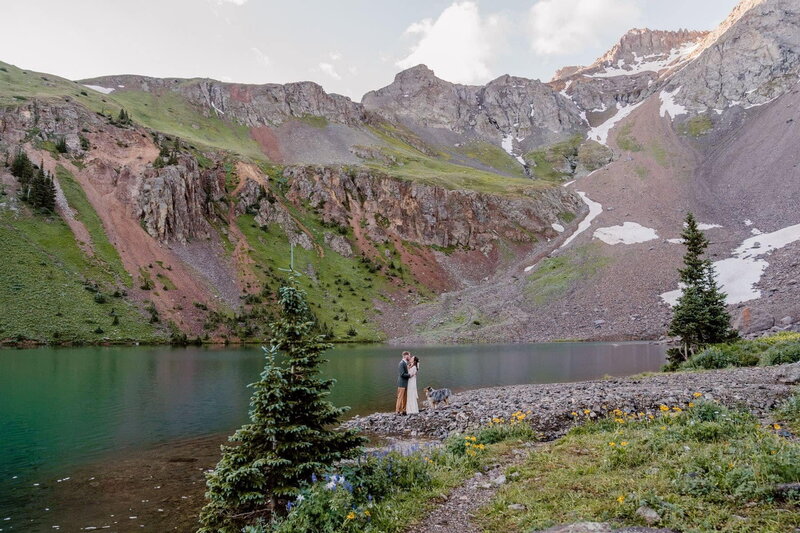 Colorado adventure elopement photographer captures a couple with their dog during an intimate ceremony at Ice Lake Basin surrounded by rugged mountain cliffs and a turquoise alpine lake.
