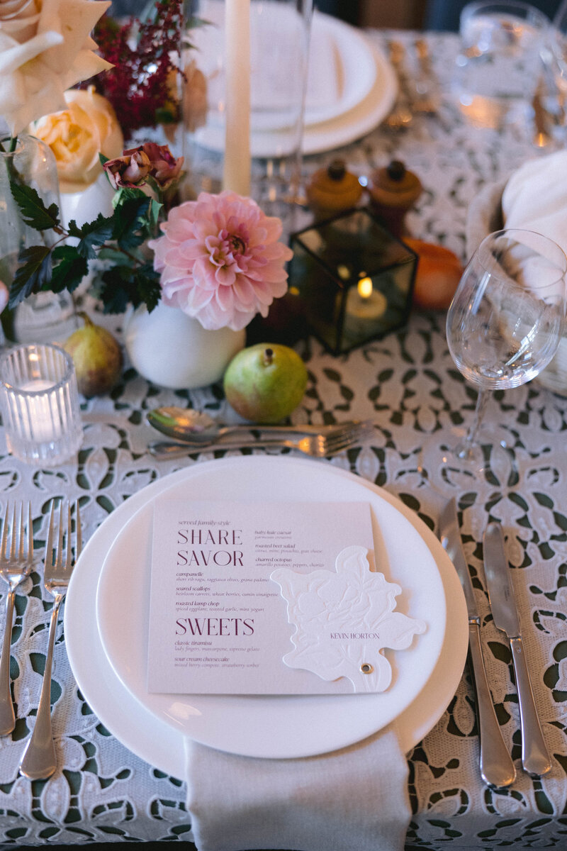 a custom wedding stationery design featuring a wedding dinner menu with a custom name tag and a flower on it on top of a white plate from alyssa amez design