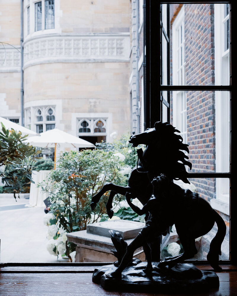 A rearing horse sculpture by a metal framed window overlooking a courtyard at a luxury london wedding.