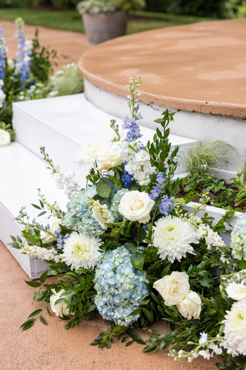 Spring wedding at WinMock at Kinderton, designed by Charming Carolina — large ground floral arrangements in dusty blue lining either side of the ceremony aisle.