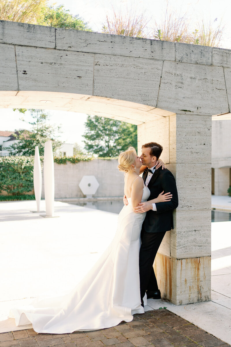 Bride and groom kissing while leaning against a stone column