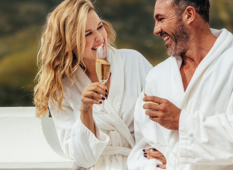 A bearded man smiling at his wife as they drink alcholic beverages.