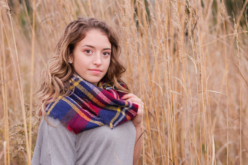 triway high school senior girl standing in tall dead grasses in fall with colorful scarf with grey shirt, far left hand in holding scarf senior is turned sideways to camera and not smiling, photographed at oak hill park in wooster ohio  photographed by jamie lynette photography canton senior photographer