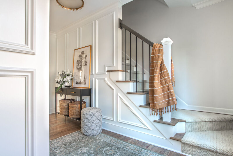 Welcoming front entryway with rust colored blanket draped over the stair railing designed by Chapin SC interior designer Haven + Harbor