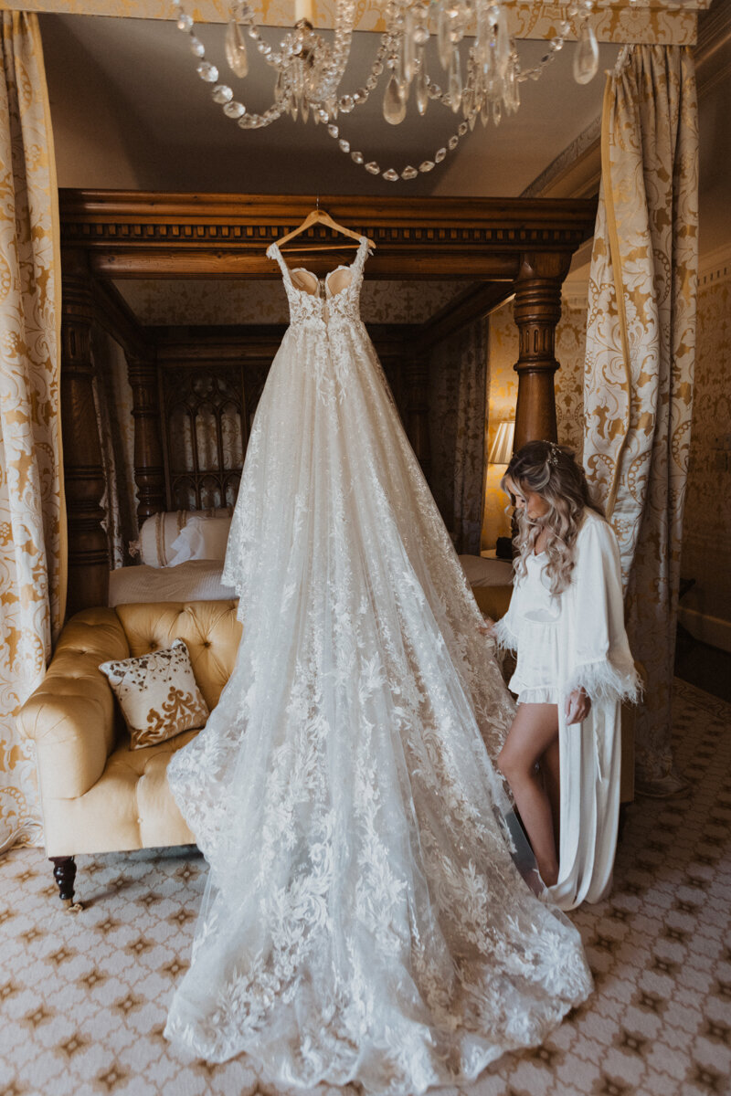 Bride looks at wedding dress in bedroom while getting ready at Dover Hall