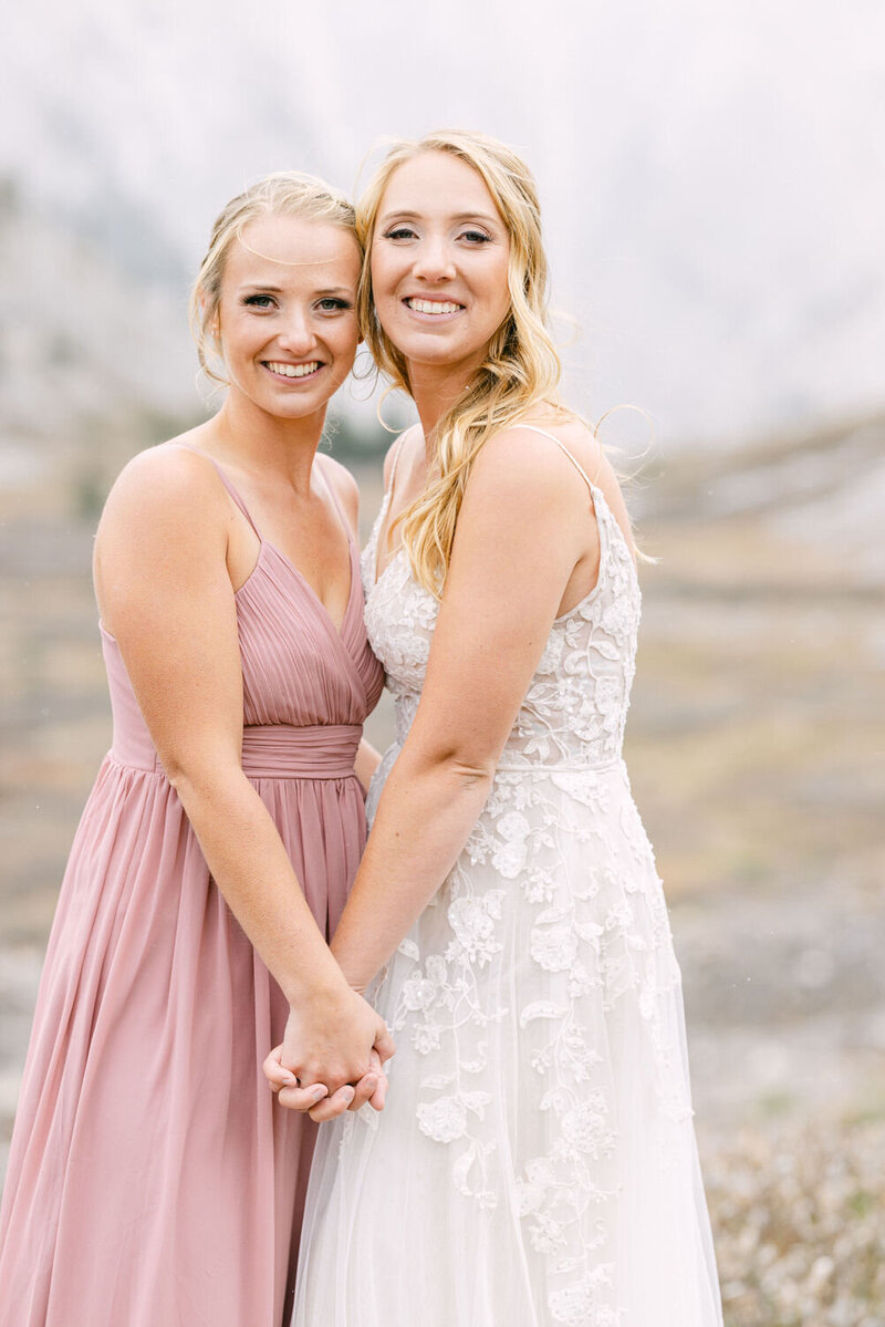 This lively portrait captures the bride and her maid of honor, who is also her sister, laughing and giggling as they look into the camera. Their genuine joy and close sibling bond shine through, adding a heartfelt touch to the wedding festivities.