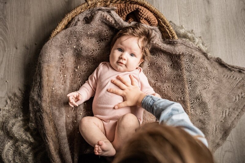6 month old baby resting on a textured blanket, gazing up with soft natural light