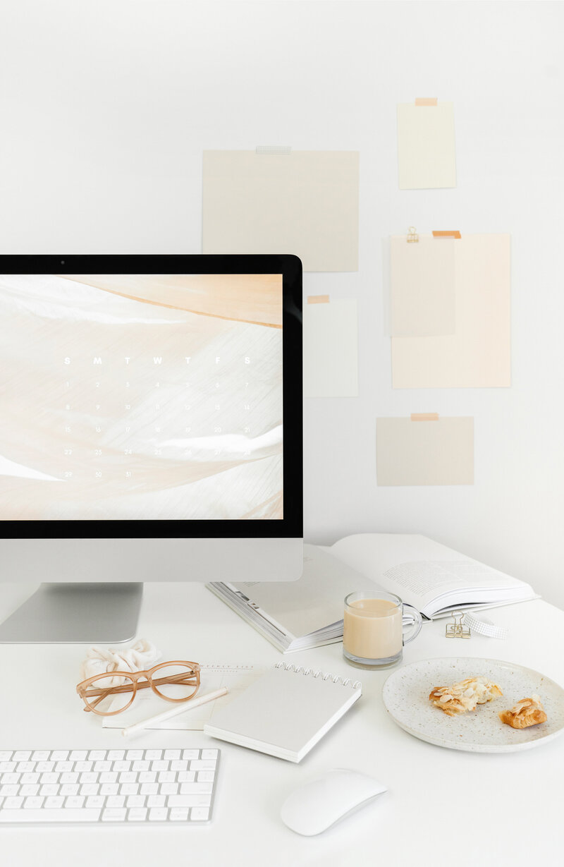 A workspace with an iMac open to Canva, coffee, pastries, and open notebooks—capturing the focus and creativity of Design Day Intensives for branding.