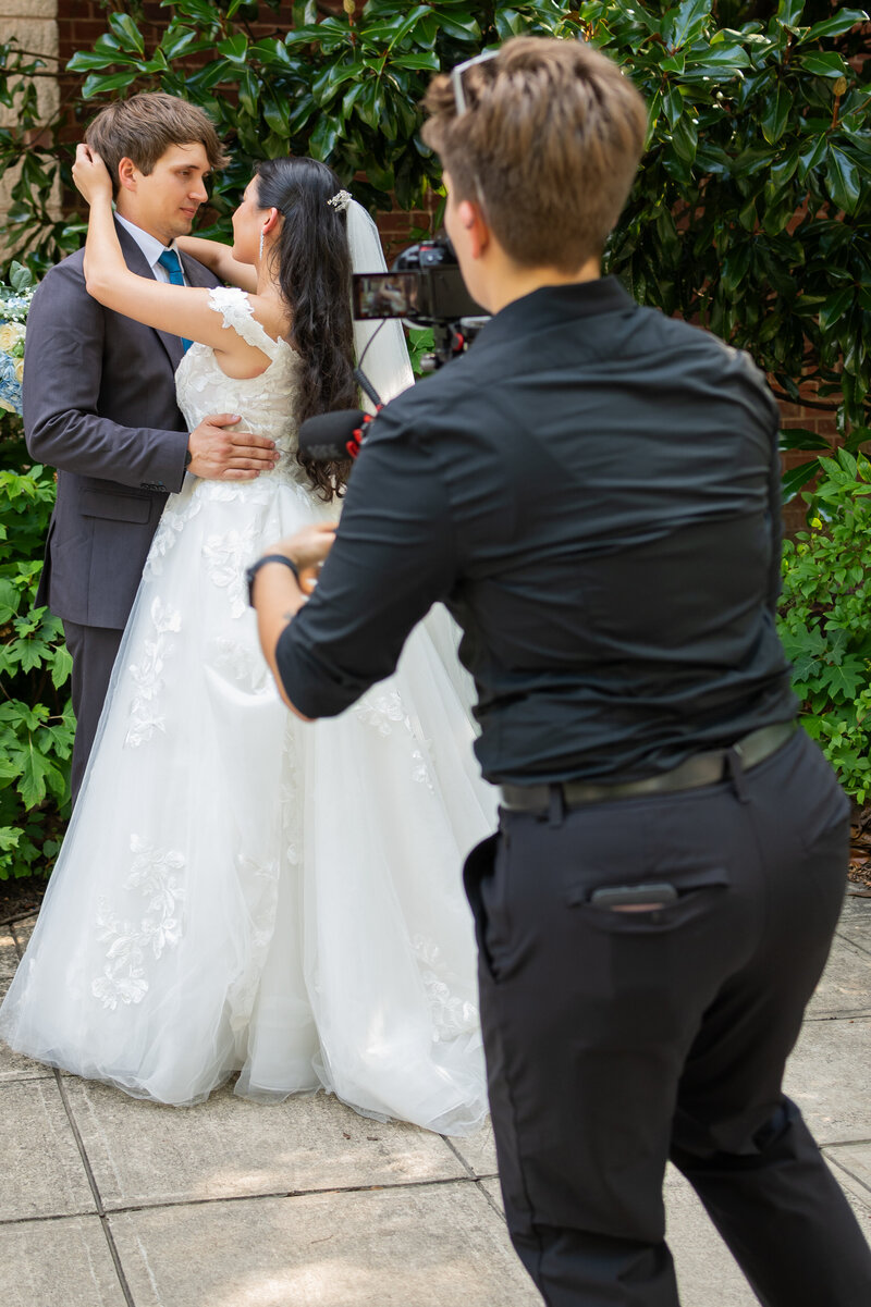 A videographer recording a couple in wedding outfits 