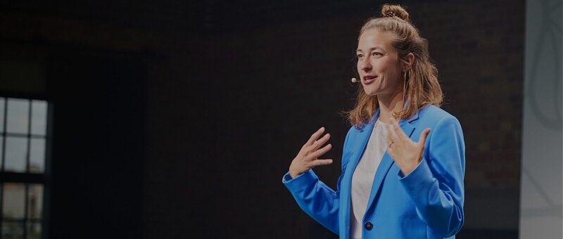 Eventmoderatorin Hanna Zöller moderiert live auf der Bühne mit Mikrofon und blauem Blazer