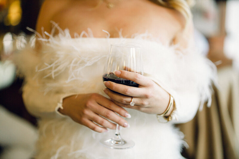 A woman wearing a white, feather dress and holding a glass of red wine.