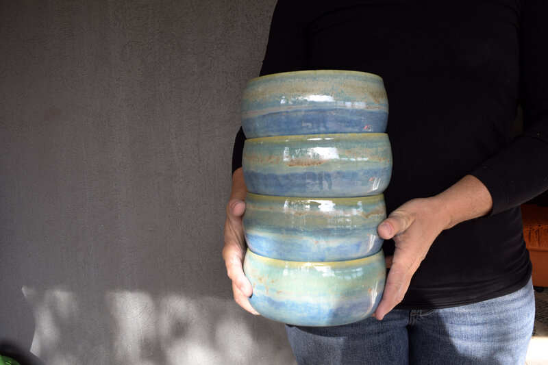 Jill holds a set of custom ceramic bowls. The four bowls are glazed with 5 different colors to make a green to blue gradient