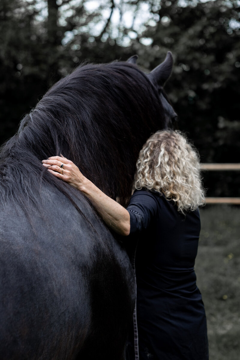 Monique communiceert met haar zwarte paard Jeltsje tijdens coaching sessie.