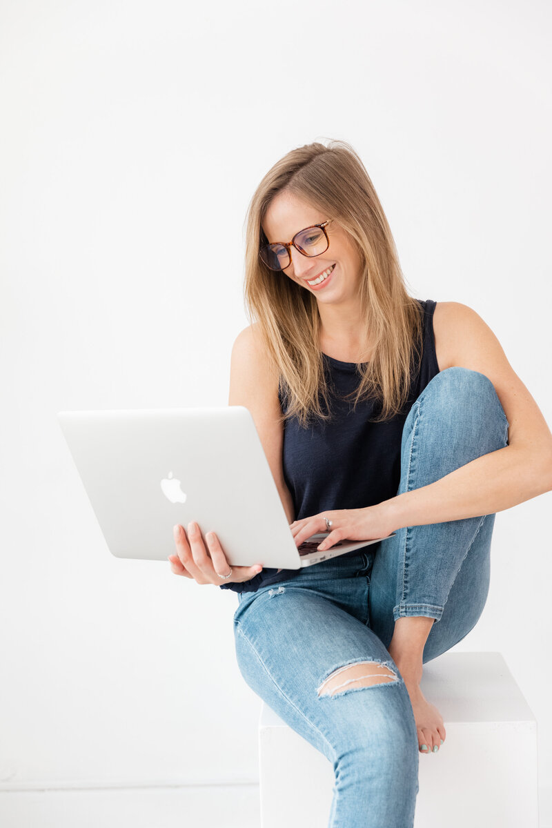 Blonde lady with glasses and blue top looking at laptop