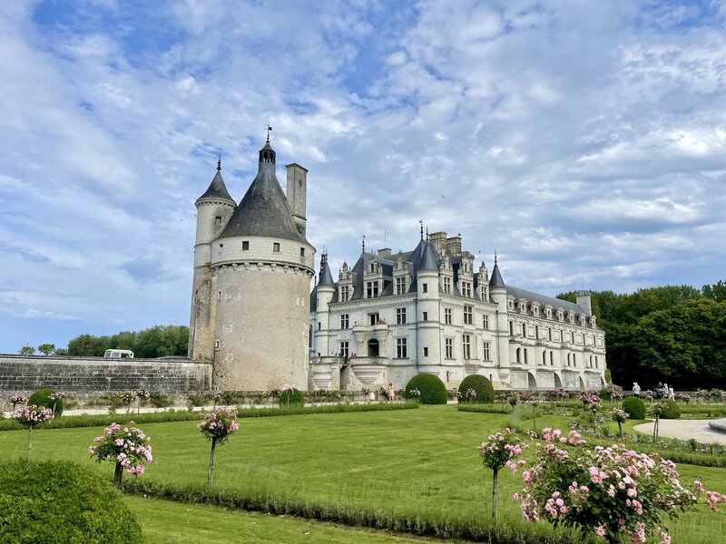 Château de Chenonceau in the Loire Valley, framed by a vibrant rose garden in the foreground, with its arches spanning the Cher River.
